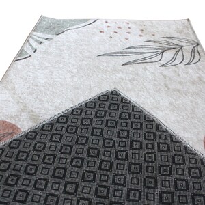May include: A beige rug with a geometric pattern and a black and white geometric pattern on the back. The rug has a floral design with brown and green accents.