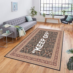 May include: A black and cream patterned rug with a white "KEEP OFF" text in the centre. The rug has a traditional floral design with a border.