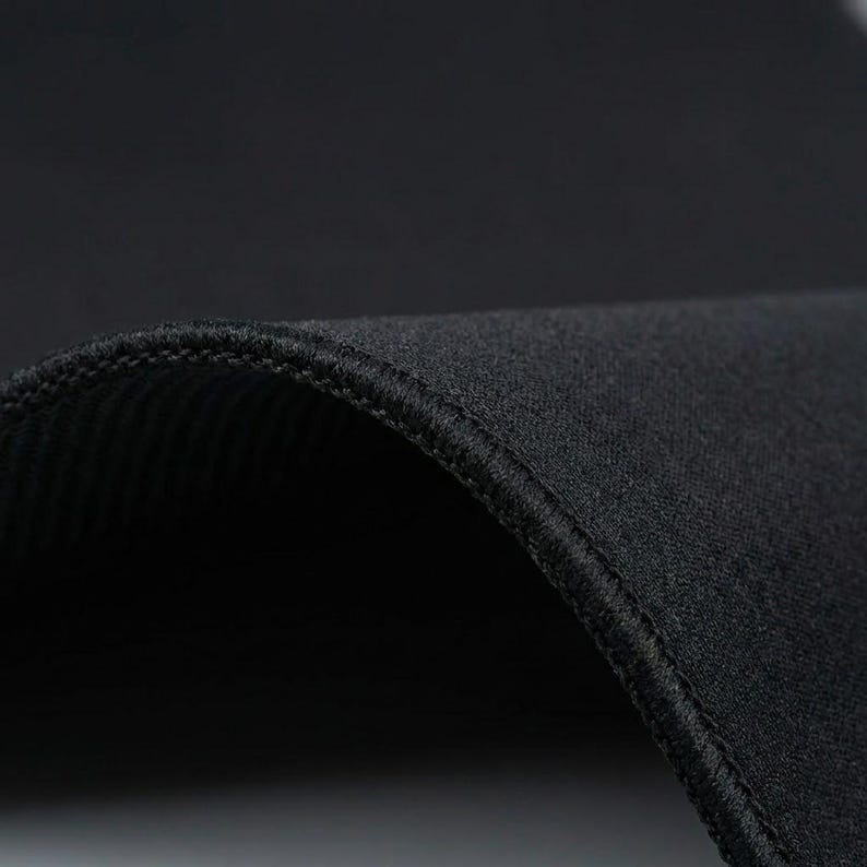 K&ouml;nnte beinhalten: Nahaufnahme eines schwarzen Stoffes mit gebogenem Rand. Der Stoff hat eine strukturierte Oberfl&auml;che und einen gen&auml;hten Rand, wodurch eine glatte, abgerundete Form entsteht. Das Bild hebt die Textur des Materials und die Qualit&auml;t der N&auml;hte hervor.