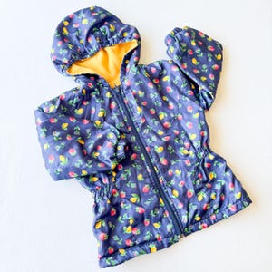 May include: A navy blue hooded jacket with a zip. The jacket is patterned with red strawberries, yellow lemons, and green leaves. The hood lining is yellow. The jacket has elastic cuffs and a drawstring waist.