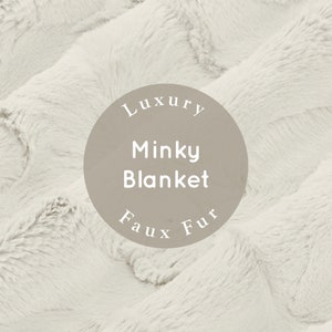 Pu&ograve; includere: Primo piano di una morbida coperta in pelliccia sintetica bianca. La coperta &egrave; testurizzata e soffice, con un'etichetta circolare che recita "Luxury Minky Blanket Faux Fur".