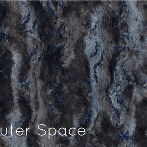 K&ouml;nnte beinhalten: Ein Pl&uuml;schstoff in einem dunkelgrauen und blauen Farbschema. Der Stoff hat eine flauschige Textur und ein wirbelndes Muster. Der Text "Outer Space" ist unten im Bild gedruckt.