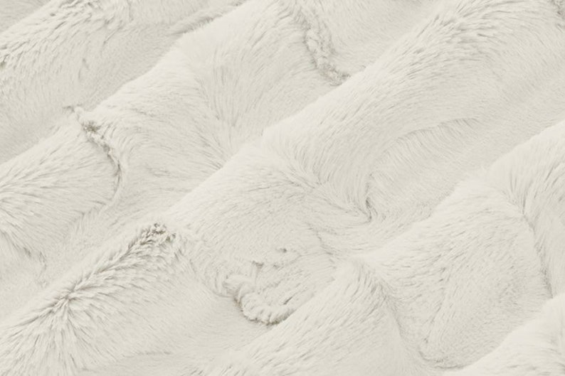 Pu&ograve; includere: Un tessuto in pelliccia sintetica bianca morbida con un motivo ondulato e testurizzato. Il tessuto &egrave; morbido e soffice, simile a una texture nuvolosa.