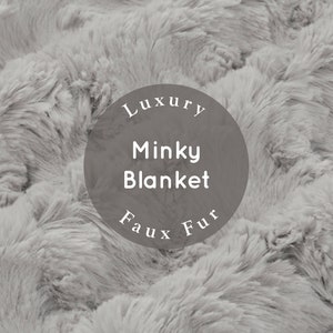 May include: A close-up of a soft, gray, faux fur blanket. The blanket has a wavy, textured pattern. The text "Luxury Minky Blanket Faux Fur" is printed on a circle in the center of the image.