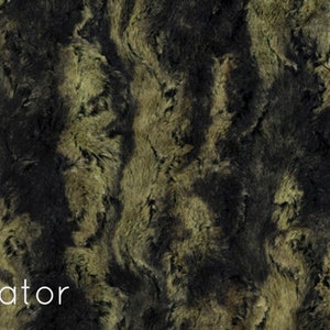 K&ouml;nnte beinhalten: Nahaufnahme eines Kunstpelzstoffes in Schwarz und Gr&uuml;n. Der Stoff hat ein welliges Muster und eine weiche, pl&uuml;schige Textur. Das Wort "Gator" ist unten im Bild in Wei&szlig; gedruckt.