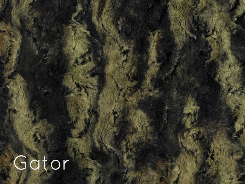 K&ouml;nnte beinhalten: Nahaufnahme eines Kunstpelzstoffes in Schwarz und Gr&uuml;n. Der Stoff hat ein welliges Muster und eine weiche, pl&uuml;schige Textur. Das Wort "Gator" ist unten im Bild in Wei&szlig; gedruckt.
