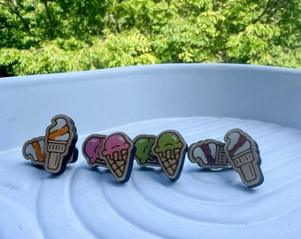 May include: Five wooden ice cream cone charms in different colors and flavors. The charms are painted with details like sprinkles, chocolate sauce, and vanilla ice cream.