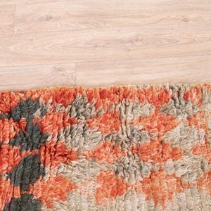 May include: Close-up of a colorful rug with a mix of orange, gray, and black tones. The rug has a textured, fluffy surface.