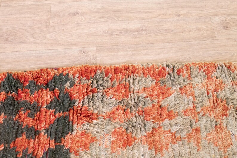 May include: Close-up of a colorful rug with a mix of orange, gray, and black tones. The rug has a textured, fluffy surface.