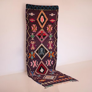 May include: A long, narrow rug with a geometric pattern in shades of pink, blue, green, yellow, and black on a dark purple background.