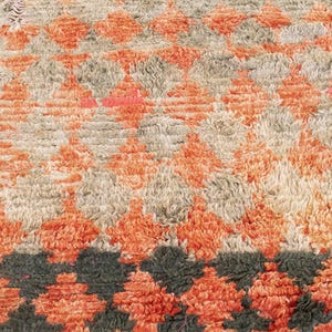 May include: A close-up of a rug with a geometric pattern in shades of orange, beige, and black. The rug has a soft, fuzzy texture.