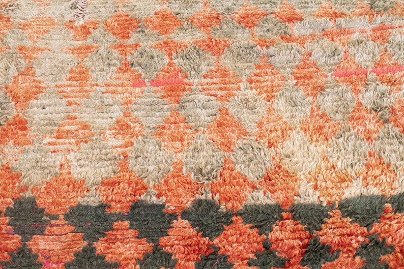 May include: A close-up of a rug with a geometric pattern in shades of orange, beige, and black. The rug has a soft, fuzzy texture.