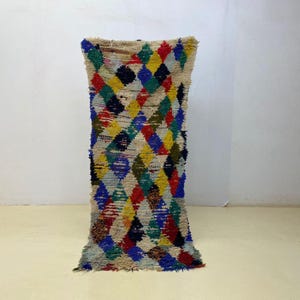 Peut inclure: Un tapis rectangulaire tissé à la main avec un motif de losanges de différentes couleurs. Le tapis présente un fond crème avec un motif répété de losanges rouges, jaunes, bleus, verts et noirs. Le tapis mesure environ 152 cm de long.