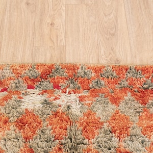 May include: A close-up of a colorful, patterned rug with orange, gray, and white tones. The rug has a textured, fluffy surface and a geometric design.