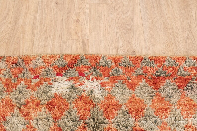 May include: A close-up of a colorful, patterned rug with orange, gray, and white tones. The rug has a textured, fluffy surface and a geometric design.