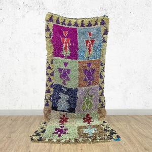 Peut inclure: Un tapis rectangulaire coloré avec un motif patchwork. Le tapis présente des carrés violets, bleus, verts et marrons, chacun avec un motif géométrique unique. Les bords du tapis sont frangés avec un mélange de couleurs, ajoutant de la texture et de l'intérêt visuel.