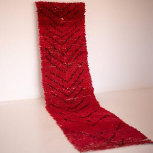 May include: A long, rectangular runner rug featuring a vibrant red base color with a repeating black chevron pattern. The rug has a thick, shaggy pile texture and is displayed in a vertical orientation, showing its full length and narrow width.