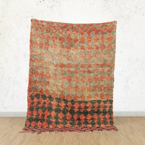May include: A vintage Moroccan rug with a geometric pattern in shades of red, orange, and black. The rug has a distressed look and is made of wool.