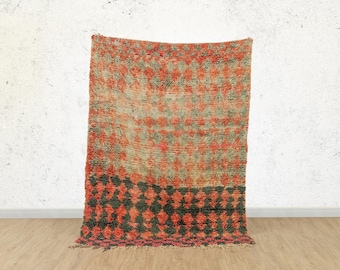 Puede incluir: Una alfombra marroquí vintage con un patrón geométrico en tonos rojos, naranjas y negros. La alfombra tiene un aspecto desgastado y está hecha de lana.