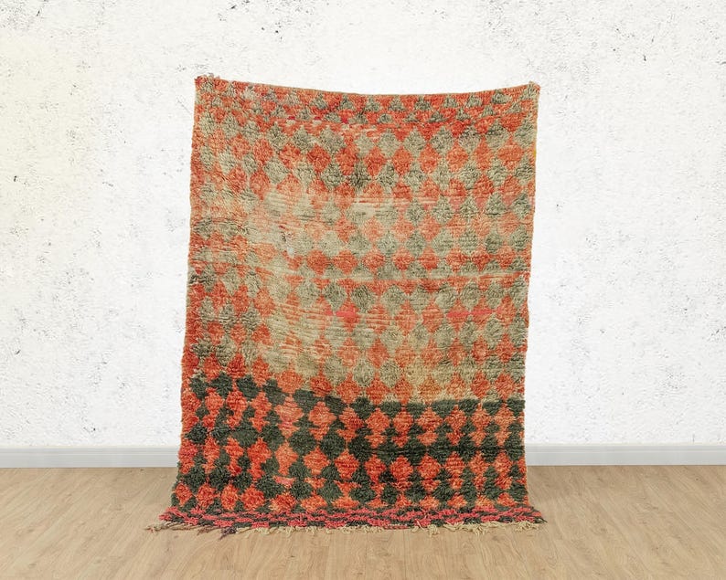 May include: A vintage Moroccan rug with a geometric pattern in shades of red, orange, and black. The rug has a distressed look and is made of wool.