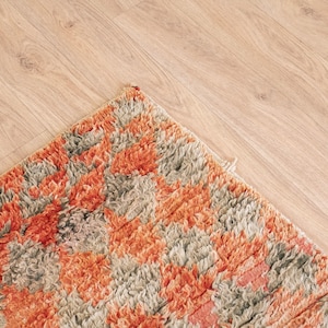 May include: Close-up of a colorful rug with a geometric pattern in shades of orange, brown, and gray. The rug has a soft, fluffy texture.