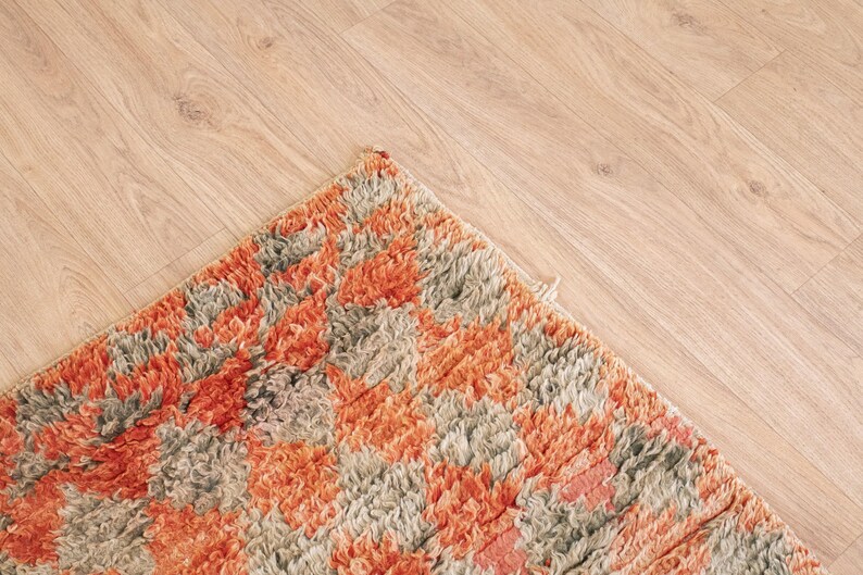 May include: Close-up of a colorful rug with a geometric pattern in shades of orange, brown, and gray. The rug has a soft, fluffy texture.