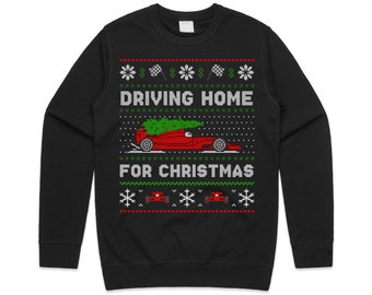 May include: Black sweatshirt with a festive design. The graphic features a red car with a Christmas tree on top, and the text "DRIVING HOME FOR CHRISTMAS" in white. The design includes snowflakes, checkered flags, and red accents.
