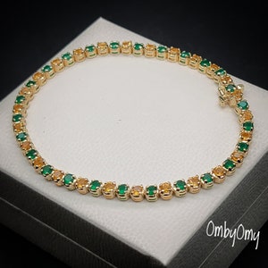 May include: A gold tennis bracelet with alternating green and yellow gemstones. The bracelet is on a white background.