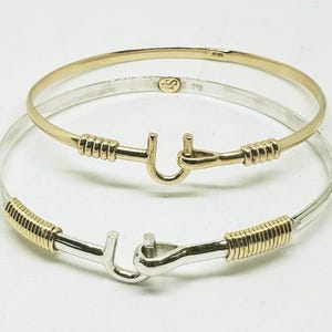May include: Two gold and silver bracelets with a hook clasp. The bracelets are stacked on top of each other. The top bracelet is gold and the bottom bracelet is silver.