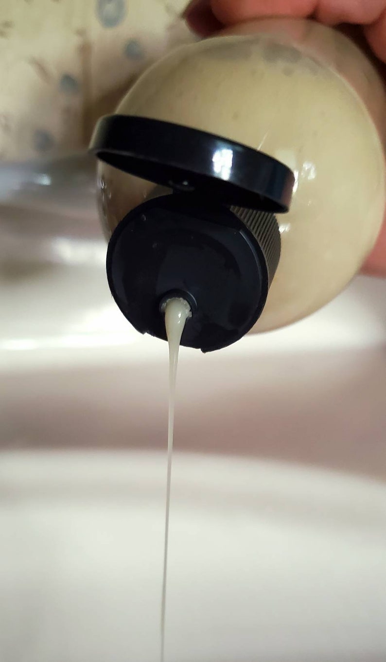 May include: A white liquid is being poured from a beige bottle with a black cap. The liquid is forming a thin stream.