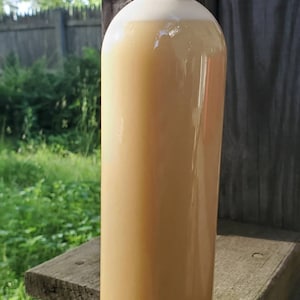 May include: A clear plastic bottle with a black lid filled with a light brown liquid. The bottle is sitting on a wooden surface.