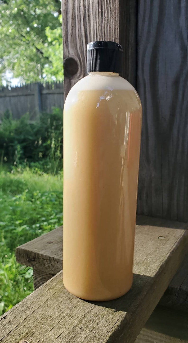 May include: A clear plastic bottle with a black lid filled with a light brown liquid. The bottle is sitting on a wooden surface.
