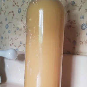May include: A clear plastic bottle with a black lid filled with a pale yellow liquid. The bottle is sitting in a white sink with a white tap in the background. There are bubbles around the bottle.