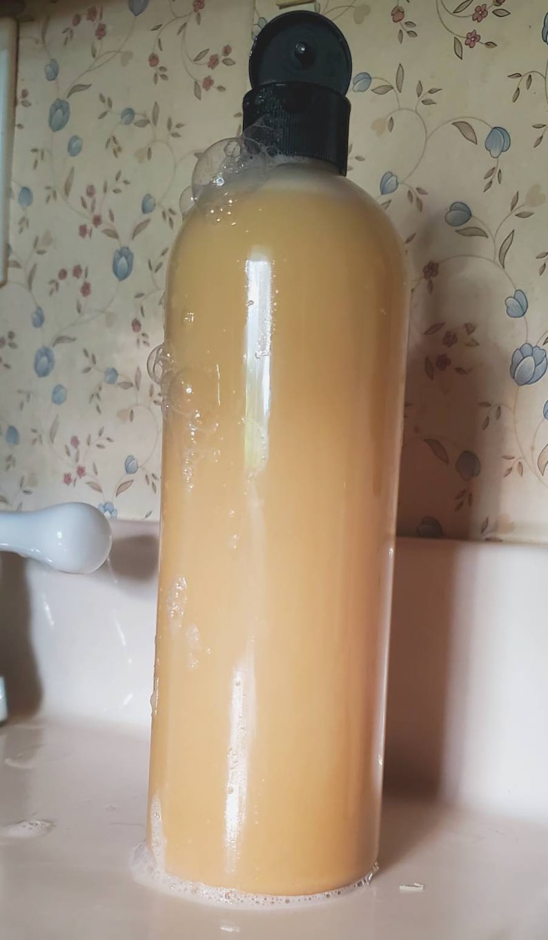May include: A clear plastic bottle with a black lid filled with a pale yellow liquid. The bottle is sitting in a white sink with a white tap in the background. There are bubbles around the bottle.