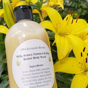 May include: A clear plastic bottle of Milk, Honey, Oatmeal & Shea Butter Body Wash by ORA European Blends. The bottle is surrounded by yellow lilies. The label lists the ingredients: Water, Goats Milk, Saponified Organic Coconut Oil, Organic Olive Oil, Organic Hemp Seed Oil, Colloidal Oats, Jojoba Oil, Citric Acid, Shea Butter, Vitamin E, Honey, Essential Oil.