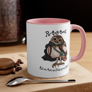 May include: White ceramic mug with a pink rim and handle. The mug features a cartoon illustration of an owl with a backpack and the text "Po-tay-toes! Boilem, Mosh em, Stick em ina Stand."