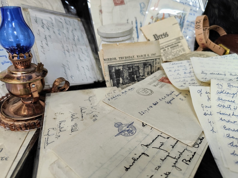May include: A collection of vintage letters, envelopes, and ephemera, including a newspaper clipping from March 6, 1947, a small glass oil lamp with a blue glass chimney, and a brown leather measuring tape.