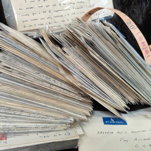 May include: A large stack of old, white envelopes with handwritten text. The envelopes are tied together with a brown leather tape measure that reads "10 METRES".