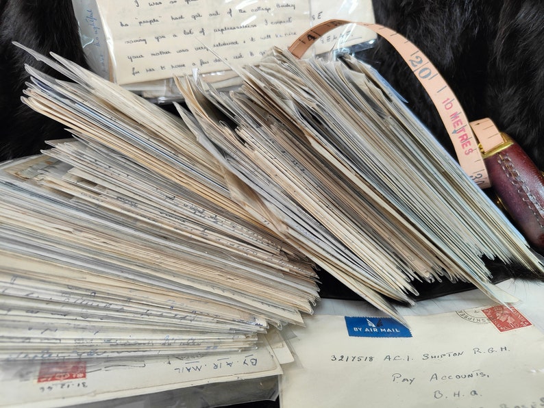 May include: A large stack of old, white envelopes with handwritten text. The envelopes are tied together with a brown leather tape measure that reads "10 METRES".