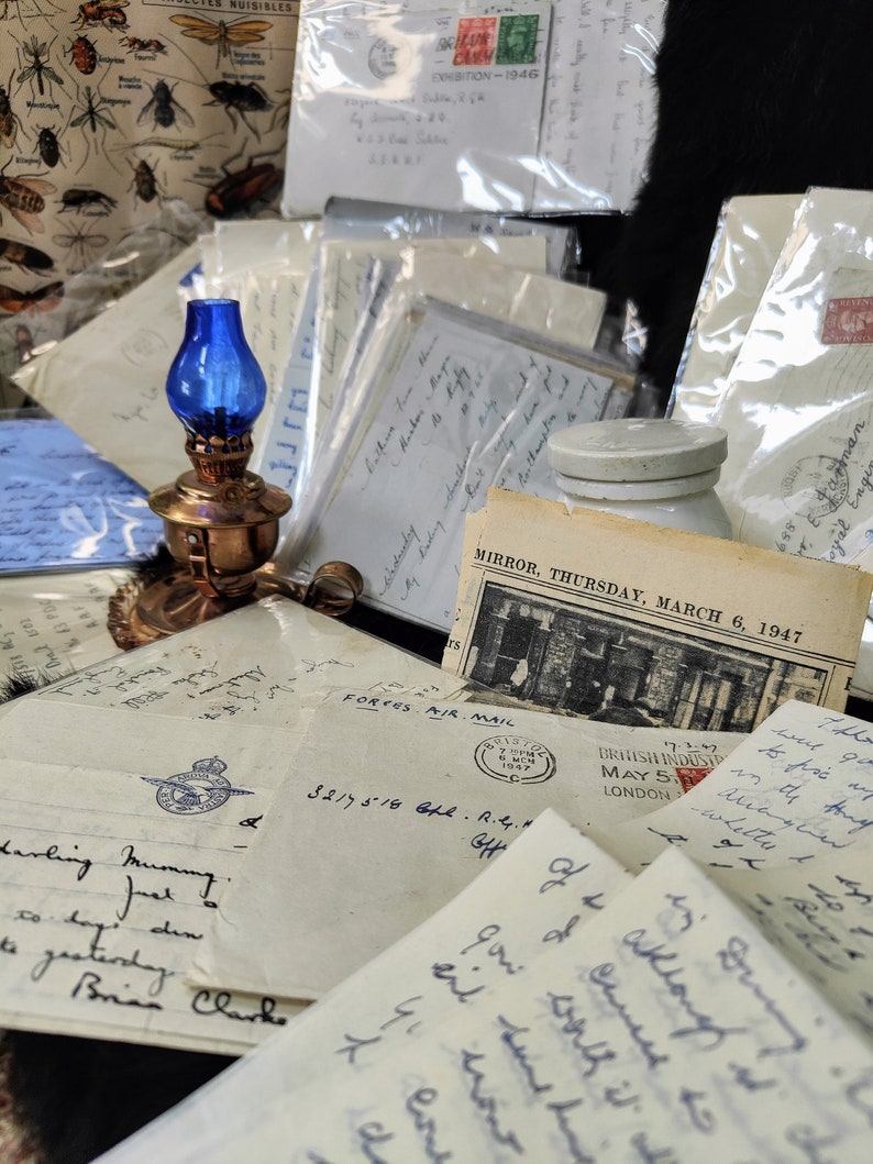 May include: A collection of vintage letters and postcards with handwritten notes, stamps, and a blue oil lamp. The letters are on aged paper with faded ink and include a stamp that reads "FORCES AIR MAIL". The postcard is from "MIRROR, THURSDAY, MARCH 6, 1947".