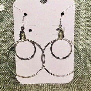 May include: A pair of silver hoop earrings with a smaller hoop inside each larger hoop. The earrings are displayed on a white card with a hole at the top for hanging.