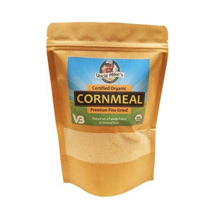May include: A brown paper bag with a clear window showing a light yellow powder inside. The bag has a label that says "Uncle Mike's Certified Organic Cornmeal Premium Fine Grind" and "Raised on a Family Farm in Central MN!"