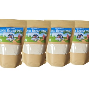 May include: Four bags of Uncle Mike's Corn Bread Mix. Each bag has a clear window showing the mix and a blue and tan label with a picture of a man and a barn. The bags are tan and sealed.