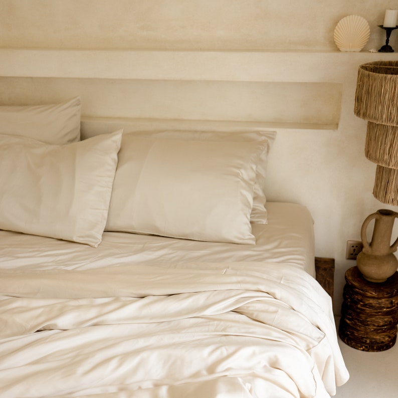 May include: A white bed with a white duvet cover and two white pillows. The bed is made and the duvet is folded back. The bed is in a room with white walls and a shelf above the headboard.
