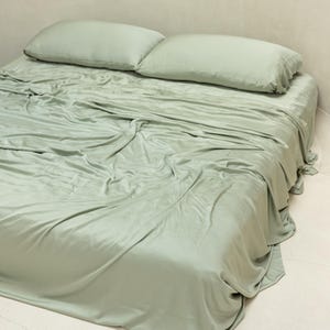 May include: A sage green bed sheet set with two matching pillowcases. The sheet is made of a soft, smooth fabric and is wrinkle-resistant.