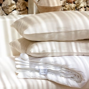 May include: A white down comforter folded on a bed with two beige pillows. The comforter has a white label with the text "Aerpom" on it.