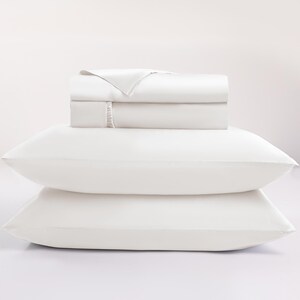 May include: A white bed sheet set with two pillows. The folded sheets are stacked on top of the pillows. The sheets and pillowcases are a solid white color. The image is well-lit and the background is white.