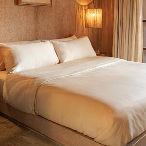 May include: A bed with cream-colored bedding, including a duvet cover and two pillows. The bed is neatly made, with the sheets and duvet cover appearing smooth and wrinkle-free. The room has a warm, inviting ambiance.