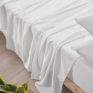 May include: A set of crisp white bed sheets draped over a mattress, featuring a smooth, soft-touch fabric with a subtle sheen. The bedding includes a fitted sheet and a flat sheet, creating a clean, uniform appearance across the surface of the bed.
