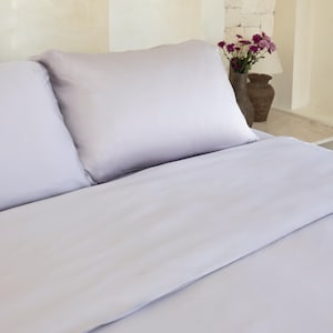 May include: A light gray bed with two pillows and a white duvet cover. The bed is made with crisp, clean linens.